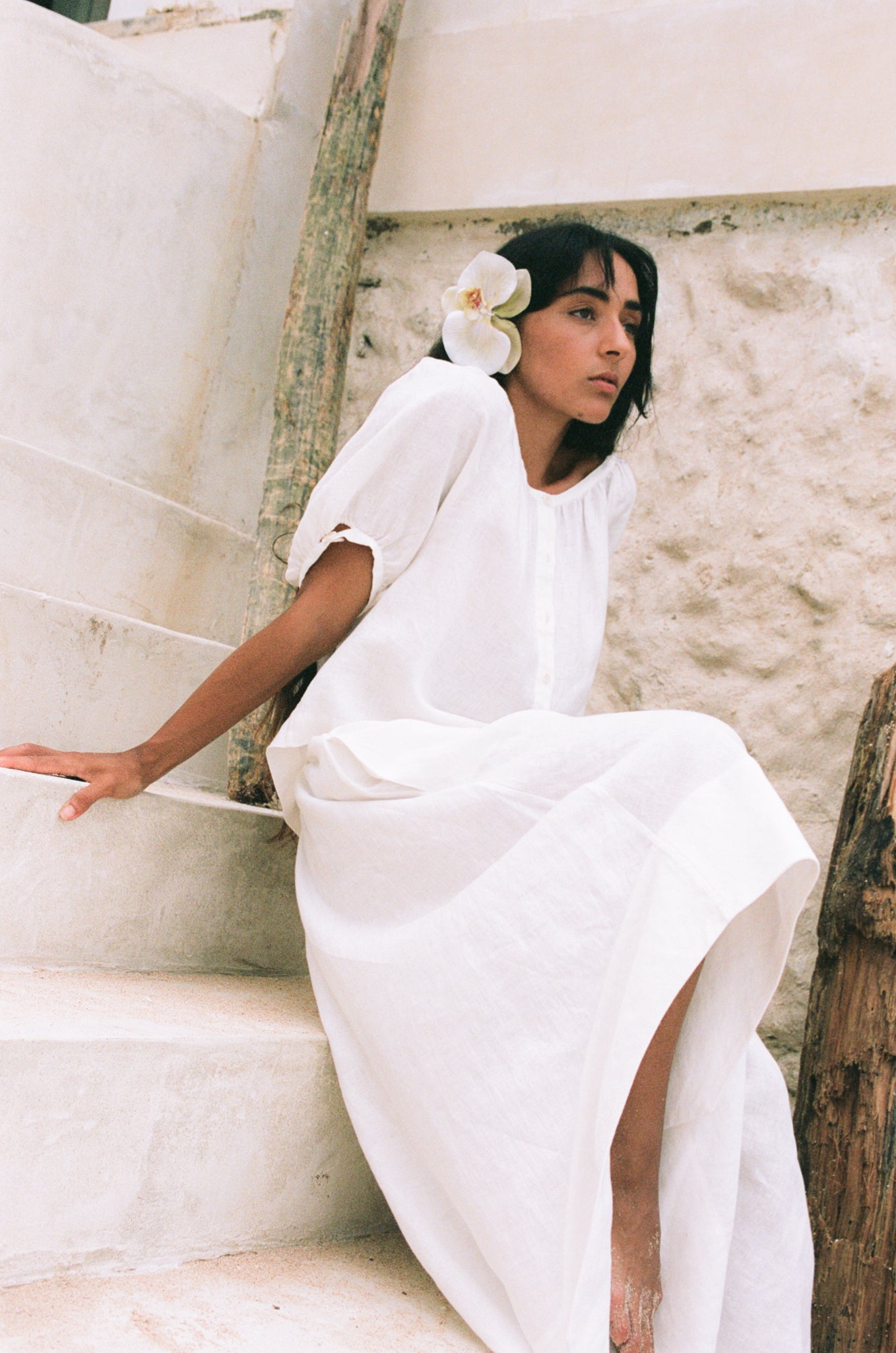 LILLY PILLY woman in a Hannah ivory linen skirt sitting on stone steps with a white flower in her hair.
